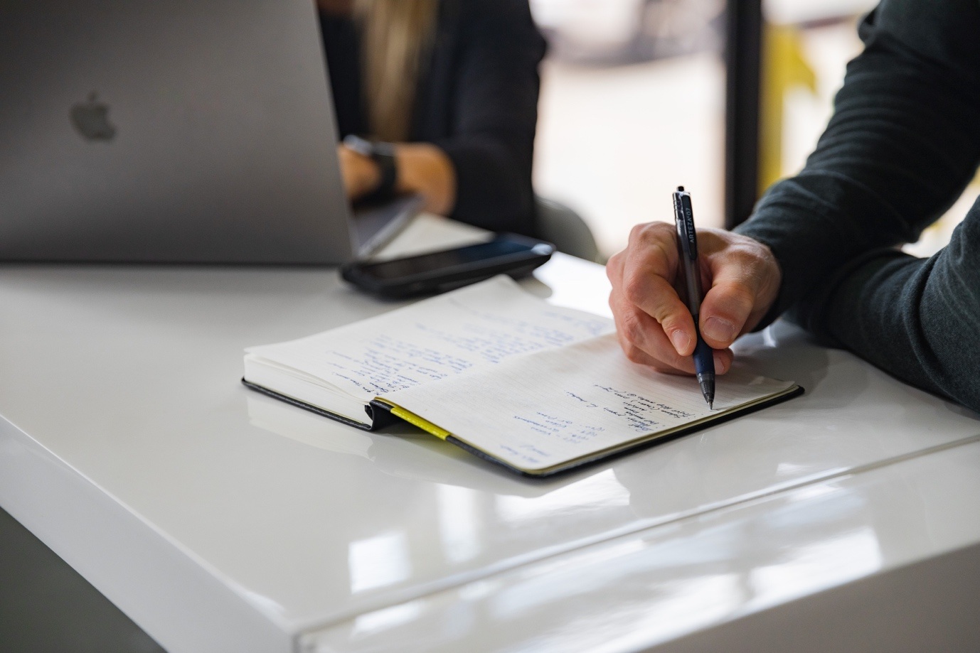 Man writing in a diary while woman works on laptop